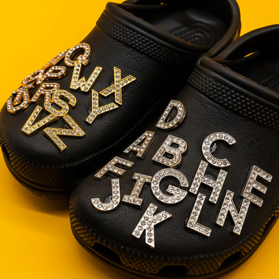 Black clogs with rhinestone letters shoe charms on a yellow background
