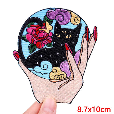 Embroidered patch with a black cat, flowers, and a hand holding a bowl held by a person.