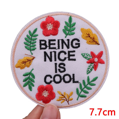 Circular patch with 'Being Nice is Cool' text surrounded by flowers and leaves, held by a hand.
