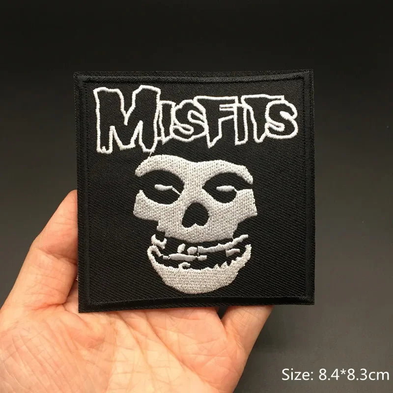 Hand holding a black and white Misfits punk band embroidered iron-on patch 8.4x8.3cm on a dark background