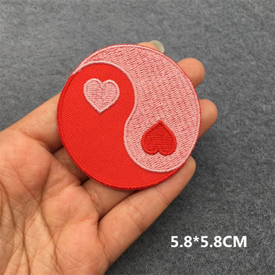 Red and pink yin yang patch with hearts held in a hand on a gray background