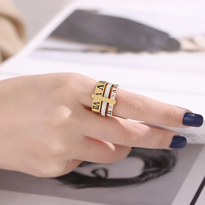 Hand wearing a gold ring with Roman numeral design on a blurred background