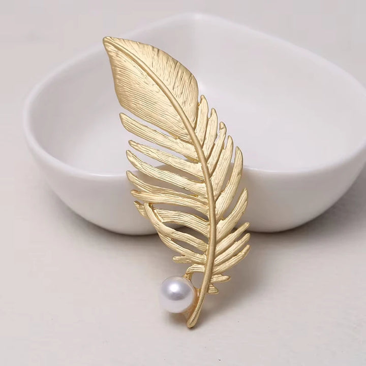 Gold leaf-shaped brooch with a pearl on a white dish
