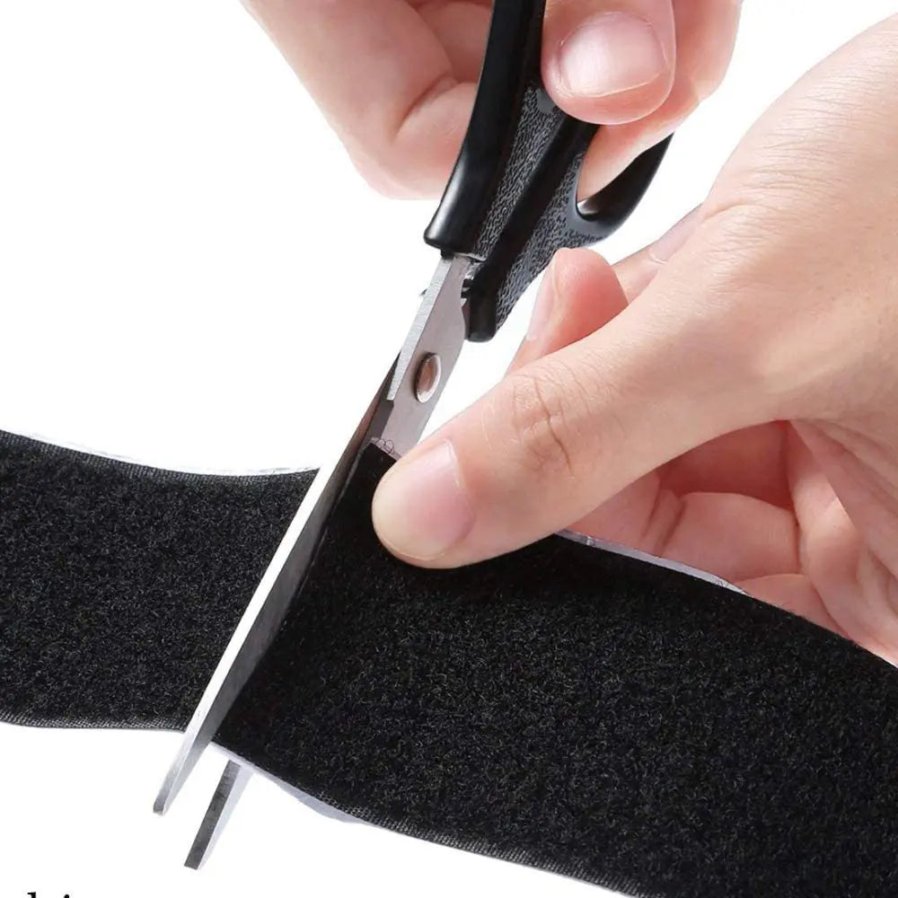 Person cutting black self-adhesive hook & loop tape with scissors on a white background