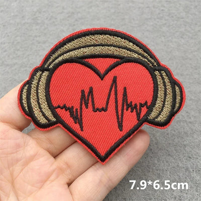 Heart-shaped patch with headphones and heartbeat line held in hand on gray background