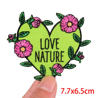 Heart-shaped patch with 'Love Nature' text and flowers, held by a finger on a white background.
