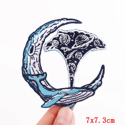 Embroidered patch of a whale and wave design held by a hand on a white background.