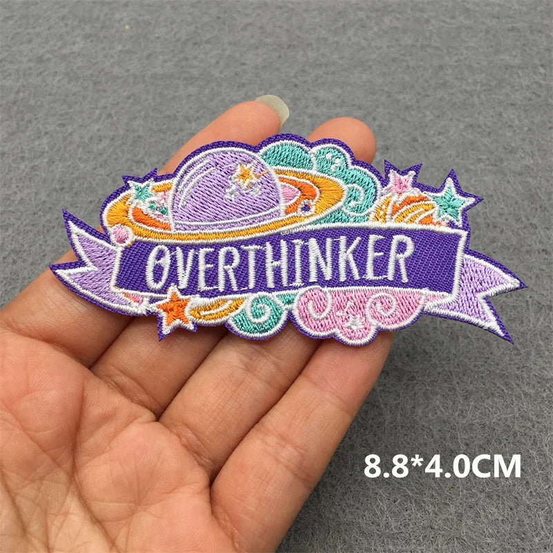 Embroidered patch with 'OVERTHINKER' text held by a hand on a gray background