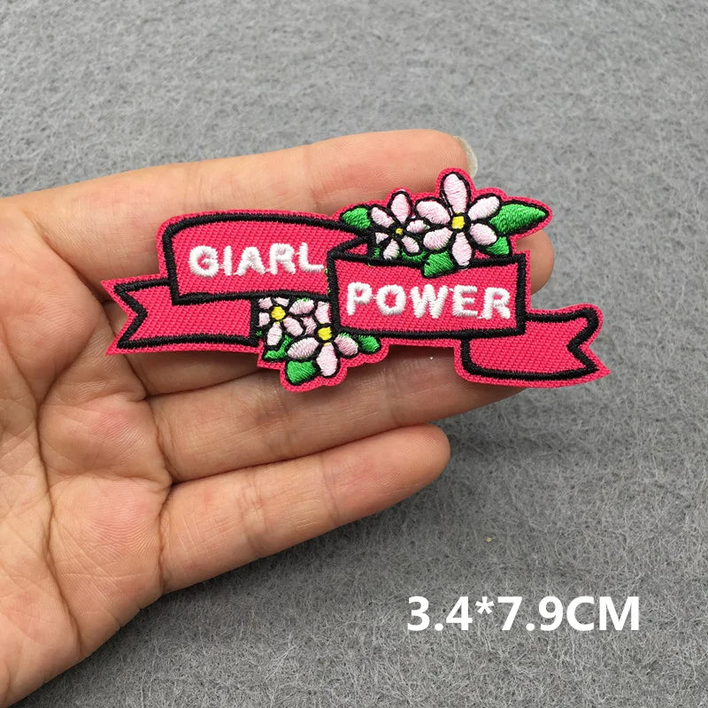 Pink patch with 'Girl Power' text held in a hand on a gray background