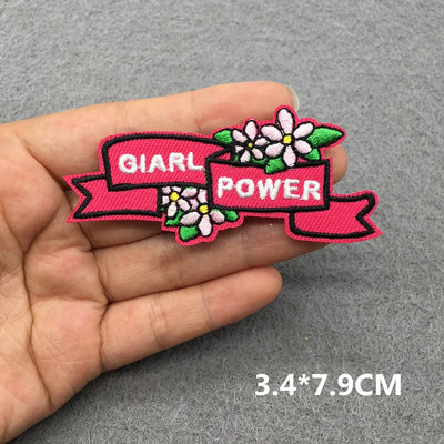 Pink patch with 'Girl Power' text held in a hand on a gray background