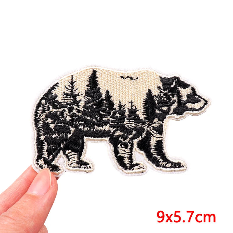 Bear-shaped patch with forest design held by a hand, size 9x5.7cm.