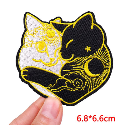 Embroidered patch of two cats with yellow outlines held by a hand on a white background.