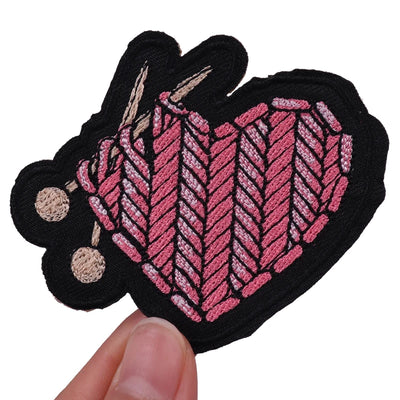 Embroidered patch with pink and black design held by a hand on a white background