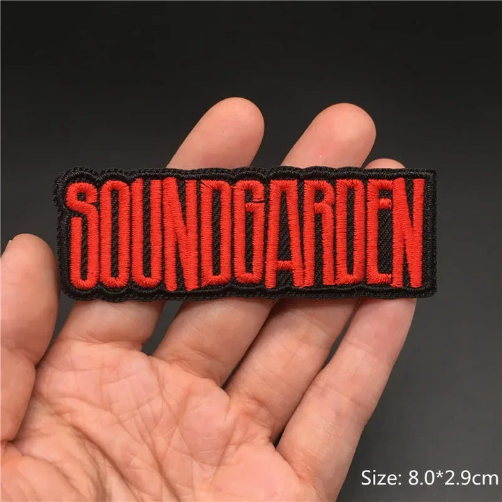 Hand holding a black and red Soundgarden embroidered iron-on patch 8x2.9cm on a dark background