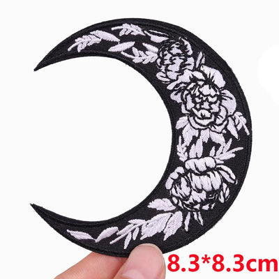 Black crescent moon-shaped patch with white floral patterns held by a hand on a white background.