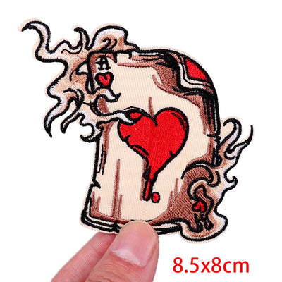 Decorative patch with a design of a face holding a heart, held by a finger on a white background.
