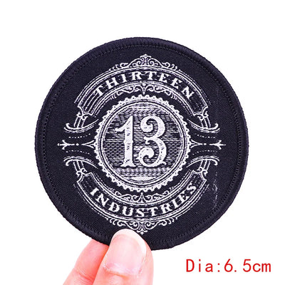 Black round patch with 'Thirteen Industries' branding held by a hand on a white background