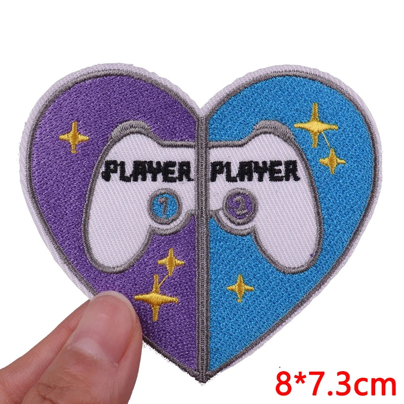 Heart-shaped patch with 'PLAYER' text and gaming controller design, held by a hand.