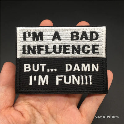 Patch with text 'I'm a bad influence but... damn I'm fun!!!' held in a hand against a dark background.