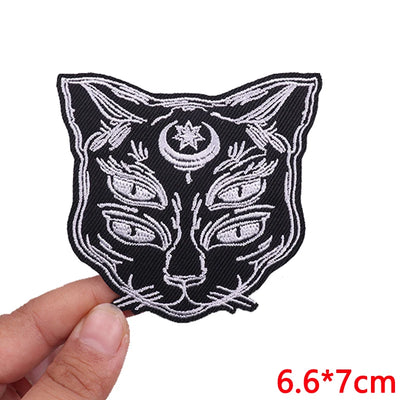 Embroidered patch of a cat's face with a star and moon symbol held by a hand on a white background.