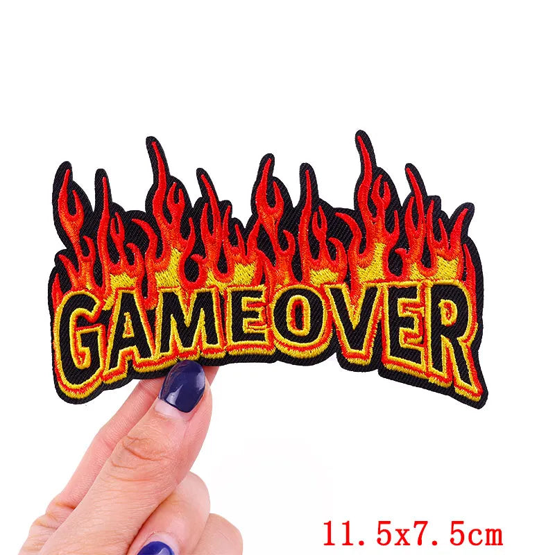Flame-themed 'GAME OVER' patch held by a hand with a white background