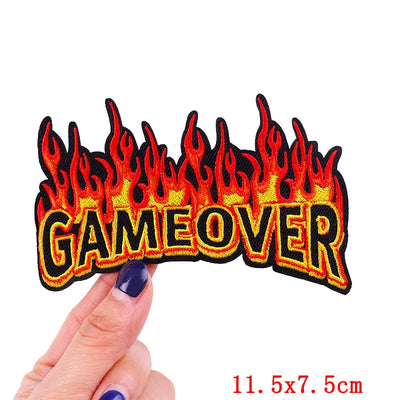 Flame-themed 'GAME OVER' patch held by a hand with a white background