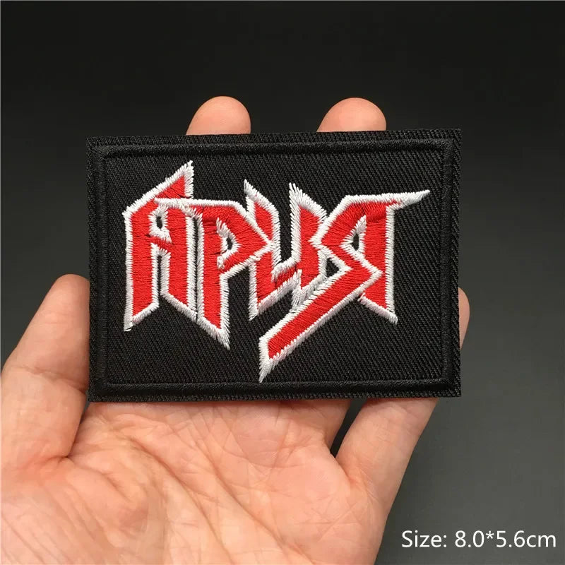 Hand holding a black red and white heavy metal logo embroidered iron-on patch 8x5.6cm on a dark background