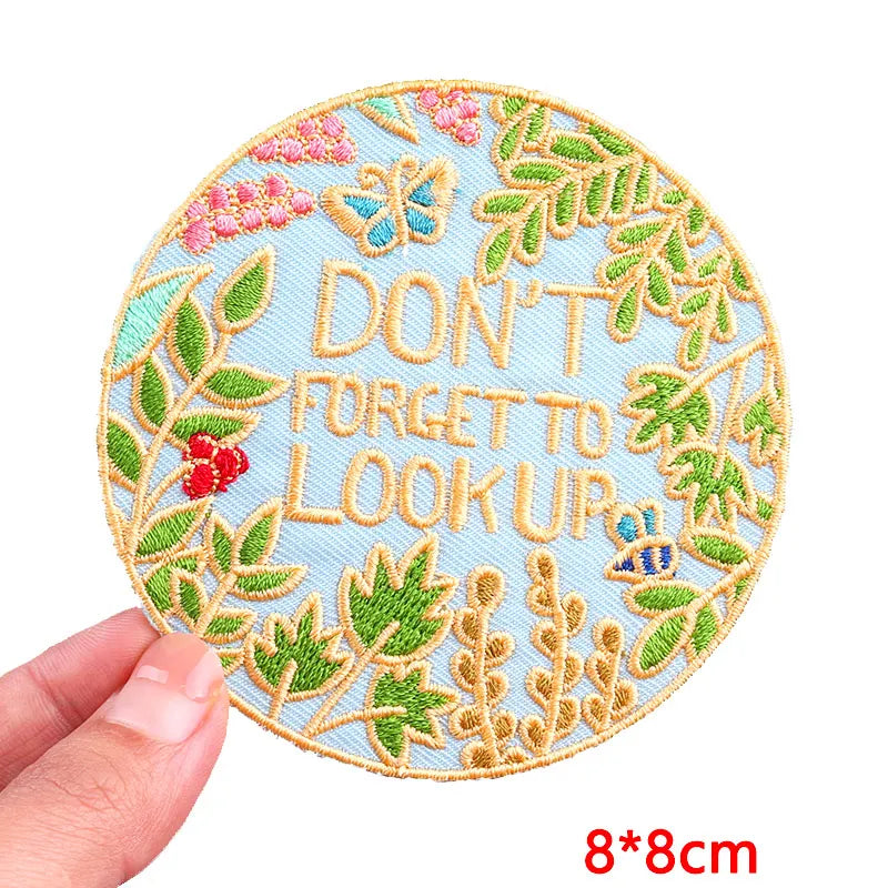 Circular embroidered patch with 'Don't forget to look up' text and floral design, held by a hand on a white background.