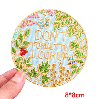 Circular embroidered patch with 'Don't forget to look up' text and floral design, held by a hand on a white background.