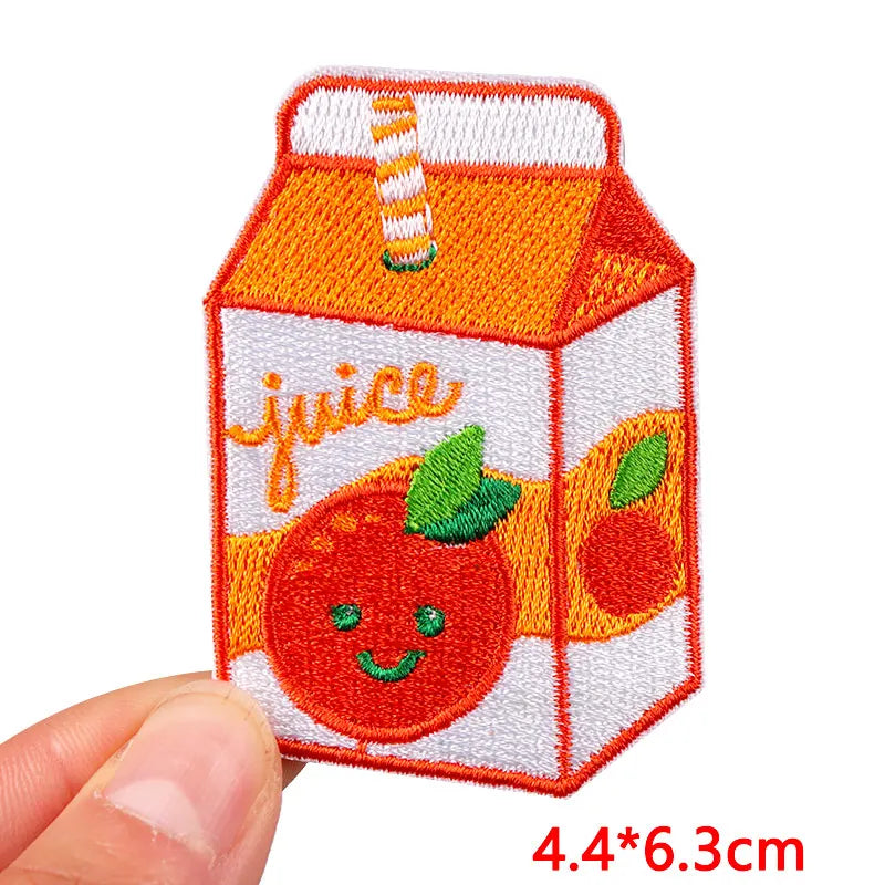 Embroidered patch of a juice box with an orange design held by a hand on a white background.