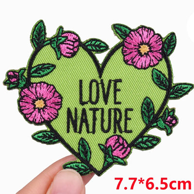 Heart-shaped patch with 'Love Nature' text and flowers, held by a hand.