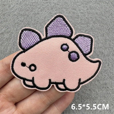 Pink cartoon-like patch with purple accents held by a hand on a gray background