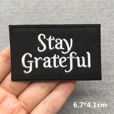 Black patch with 'Stay Grateful' text held in a hand against a gray background