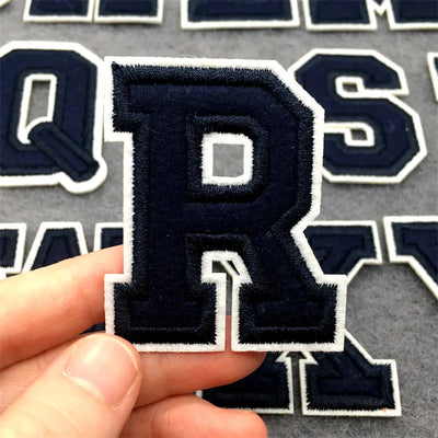 Navy letter 'R' patch held by a hand with more letter patches in the background.