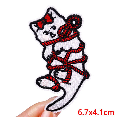 Embroidered patch of a cat tied with red rope held by a hand on a white background.