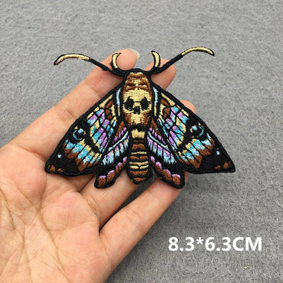 Colorful butterfly patch held by a hand on a gray background with size label '8.3*6.3CM'.