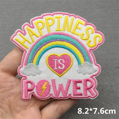 Embroidered patch with rainbow and text 'Happiness is Power' held in a hand against a gray background.