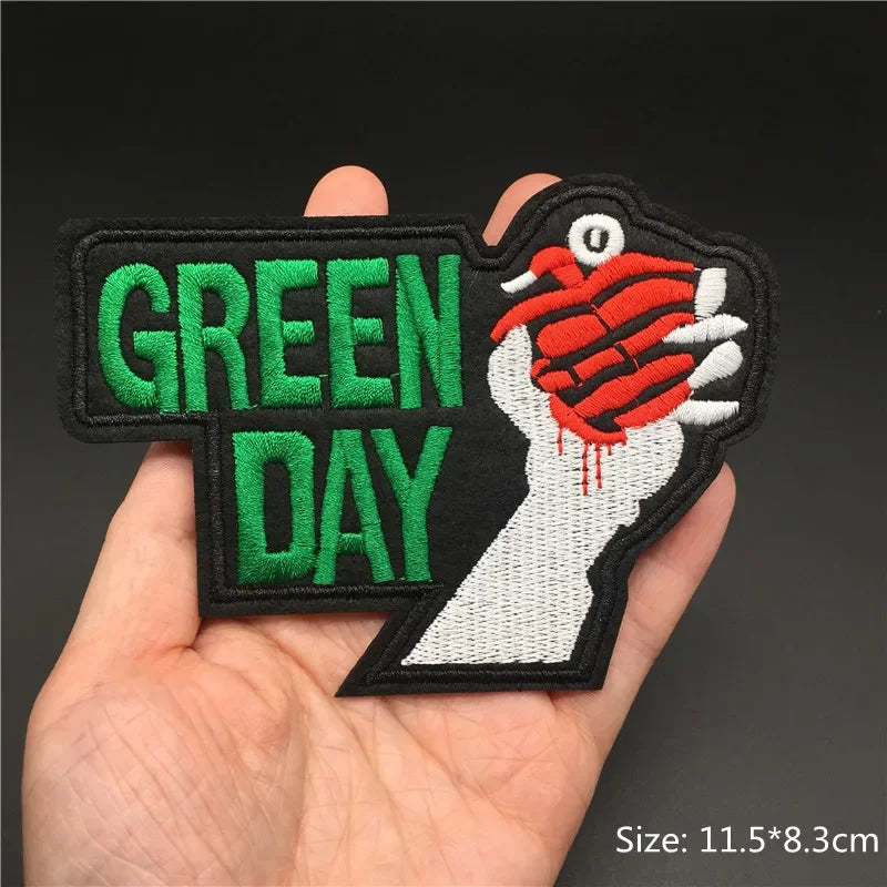 Hand holding a Green Day heart grenade embroidered iron-on patch 11.5x8.3cm on a dark background