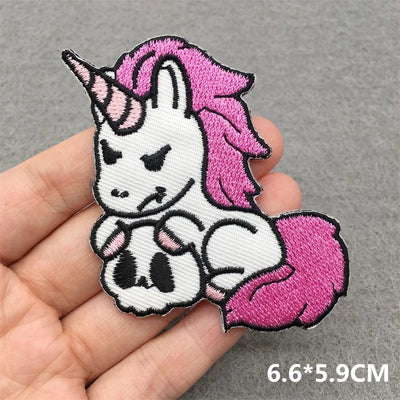 Unicorn-shaped patch with pink hair and tail held by a hand on a gray background