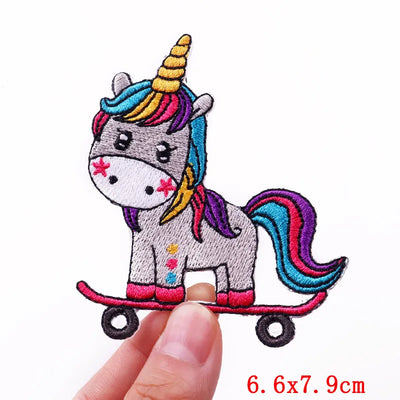 Unicorn on a skateboard patch held by a finger with dimensions 6.6x7.9cm.