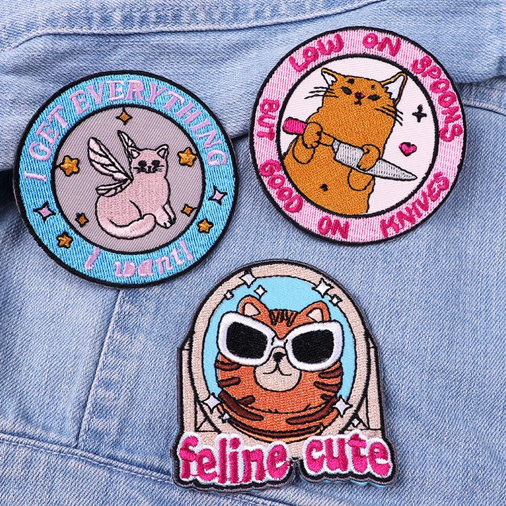 Three cat-themed patches on a denim background