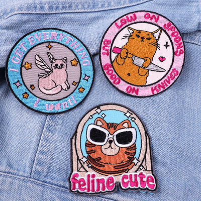Three cat-themed patches on a denim background