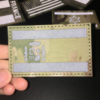 Multicam patch with a flag design held by a hand on a dark background