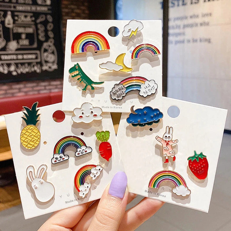 Set of colorful enamel pins on display cards held by a hand with purple nail polish.
