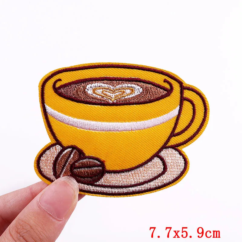 Embroidered patch of a coffee cup with a heart design held by a hand on a white background.