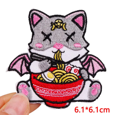 Embroidered patch of a cat eating ramen with pink accents, held by a hand.