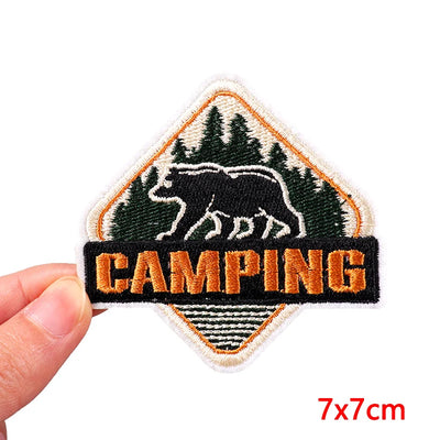 Embroidered patch with bear and 'Camping' text held by a hand, on a white background.