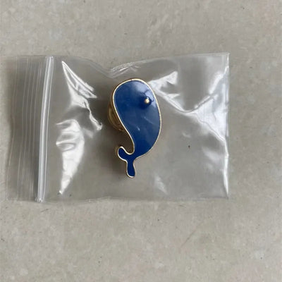 Blue whale-shaped pin in a clear plastic bag on a beige surface