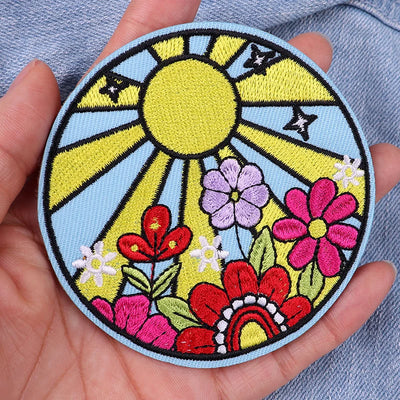 Colorful embroidered patch with flowers and a sun held in a hand.