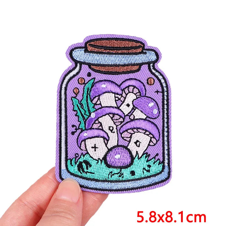 Embroidered patch of mushrooms in a jar held by a hand with size label.